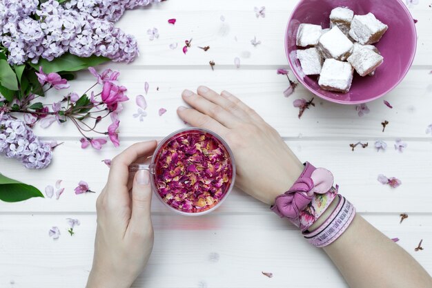 POV Ansicht einer Person mit rosa Armbändern, die eine Tasse voller Blütenblätter halten