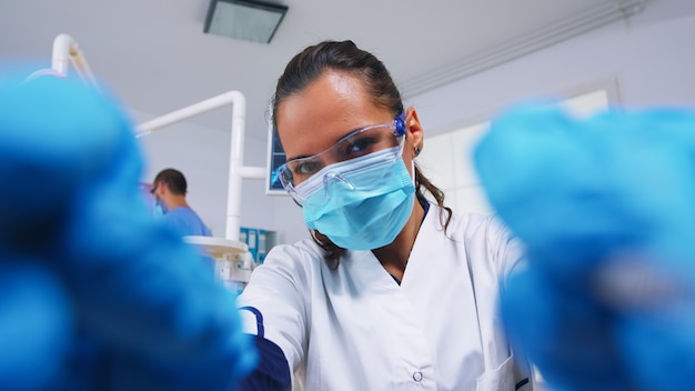 POV eines Patienten in einer Zahnklinik, der auf einem Operationsstuhl sitzt, während ein professioneller Zahnarzt mit Handschuhen während der Untersuchung in einer modernen Klinik mit sterilisierten Instrumenten arbeitet