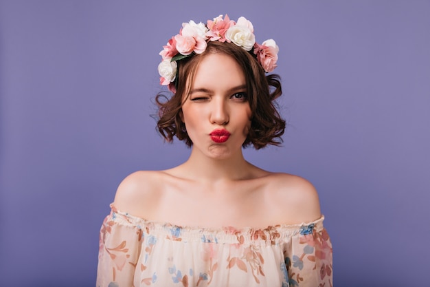 Prächtiges weißes weibliches Modell mit Blumen im stehenden Haar. Sinnliches kurzhaariges Mädchen, das mit küssendem Gesichtsausdruck aufwirft.