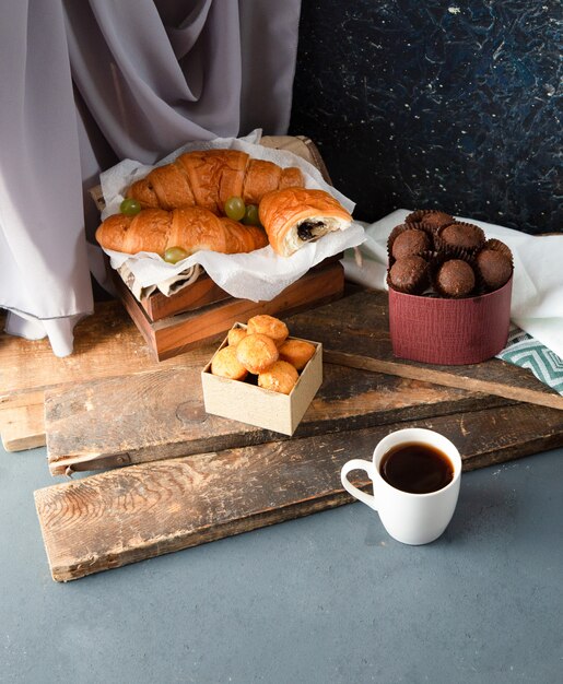 Pralinen, Muffins, Croissants und eine Tasse Kaffee auf dem blauen Tisch