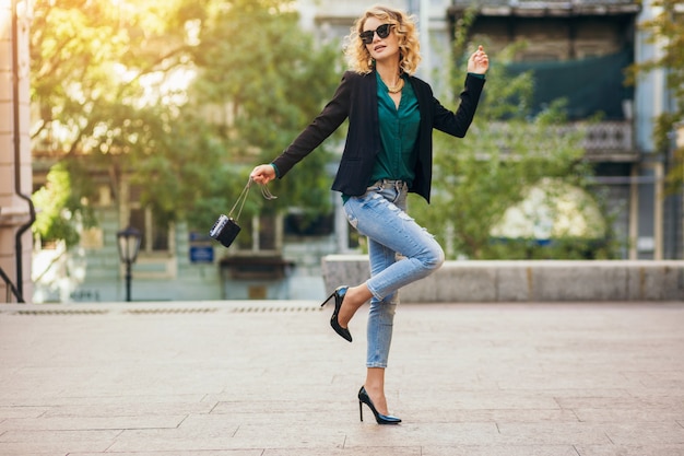 Preety stilvolle Frau, die in Blue Jeans mit Jacke und grüner Bluse auf der Straße geht, Modeaccessoires, eleganter Stil, Modetrends des Frühlings