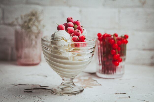 Preiselbeeren und Eiscreme in einer Glasschale auf einer weißen Struktur. Seitenansicht.