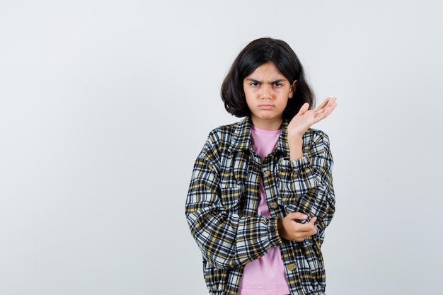 Preteen Mädchen, das die offene Handfläche in Hemd, Jacke und unzufriedener Seite ausbreitet. Vorderansicht.