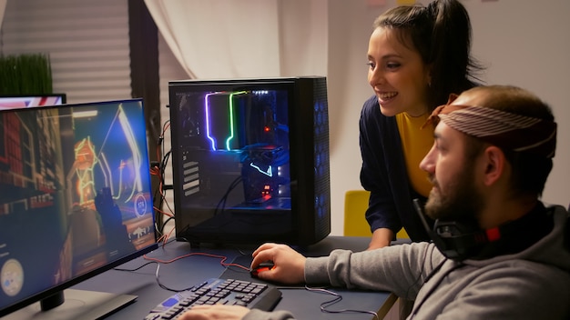 Pro Gamer-Paar, das ein Ego-Videospiel auf einem leistungsstarken Computer mit professionellen Kopfhörern spielt. Videospieler-Streaming-Gameplay-Cyber-Spiel, das auf einem Gaming-Stuhl mit RGB-Ausrüstung sitzt