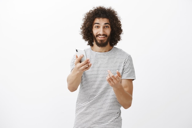 Probieren Sie es aus, Sie werden ein neues Gadget mögen. Freundlicher gutaussehender erwachsener Mann im gestreiften T-Shirt, Smartphone in Richtung ziehend