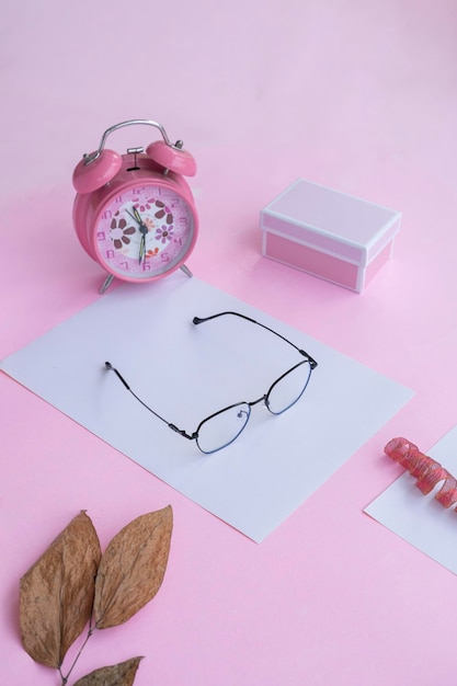Produktpräsentation der minimalistischen konzeptidee, quadratische brille, geschenkbox, uhr und trockene blätter auf rosafarbenem papierhintergrund Premium Fotos