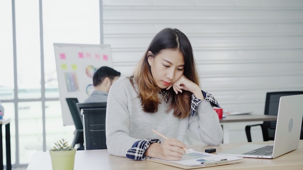 Professionelle asiatische Geschäftsfrau, die in ihrem Büro über Laptop arbeitet.