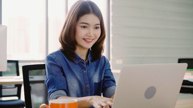 Professionelle asiatische Geschäftsfrau, die in ihrem Büro über Laptop arbeitet.