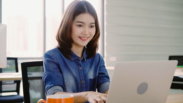 Professionelle asiatische Geschäftsfrau, die in ihrem Büro über Laptop arbeitet.