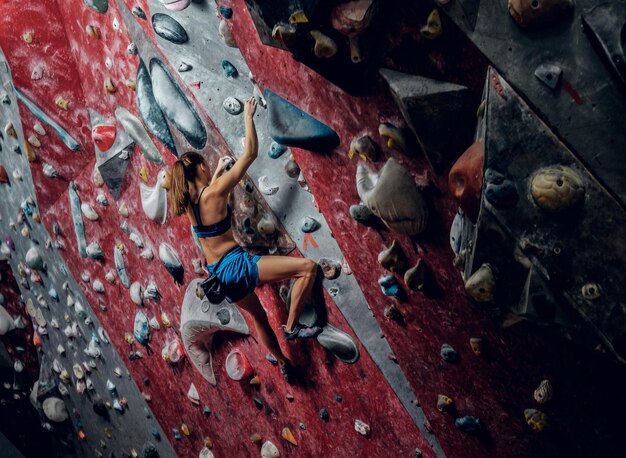 Professionelle Kletterin an einer Boulderwand im Innenbereich.