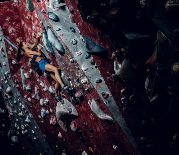 Professionelle Kletterin an einer Boulderwand im Innenbereich.