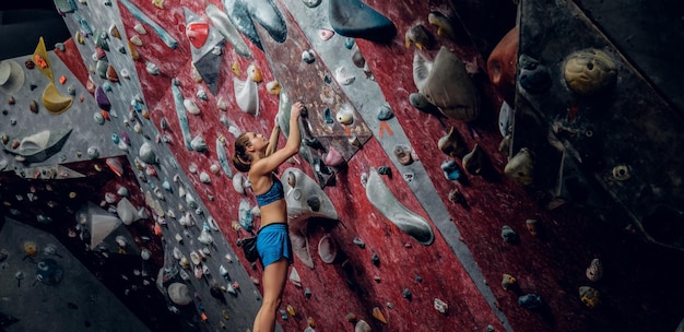 Professionelle kletterin an einer boulderwand im innenbereich.