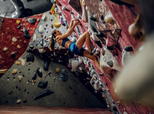 Professionelle Kletterin an einer Boulderwand im Innenbereich.