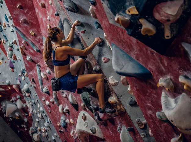 Professionelle Kletterin an einer Boulderwand im Innenbereich.