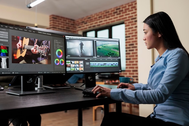 Kostenloses Foto professioneller asiatischer videoeditor, der an einem arbeitsplatz mit mehreren monitoren sitzt und gleichzeitig die qualität von filmmaterial mithilfe fortschrittlicher software verbessert. teamleiter des postproduktionshauses, der filmbilder bearbeitet.