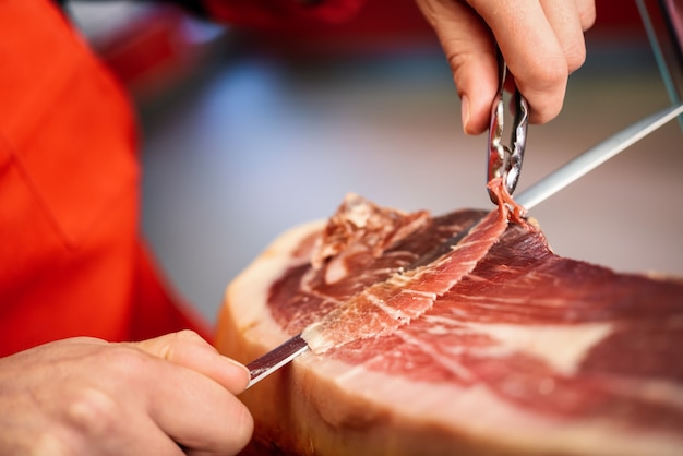 Professioneller Cutter, der Scheiben aus einem ganzen Knochen-Serranoschinken schnitzt