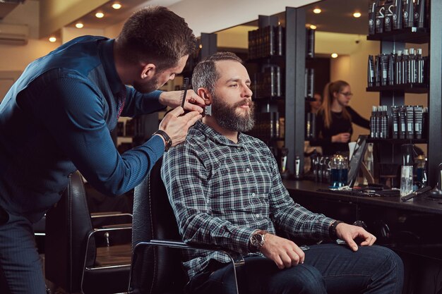 Professioneller Friseur, der mit einem Kunden in einem Friseursalon arbeitet. Bart stylen mit Trimmer.