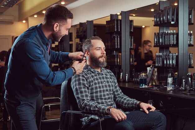 Professioneller Friseur, der mit einem Kunden in einem Friseursalon arbeitet. Bart stylen mit Trimmer.