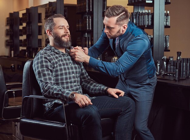 Professioneller Friseur, der mit einem Kunden in einem Friseursalon arbeitet. Bart stylen mit Trimmer.