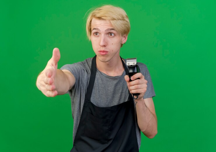 Kostenlose Foto professioneller friseurmann in der schürze, der trimmer hält, der hand macht, das grußgeste macht