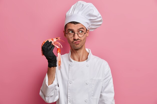 Professioneller Koch kocht Meeresfrüchte, gesundes vegetarisches Essen, hält Krebse, trägt weiße Kochuniform