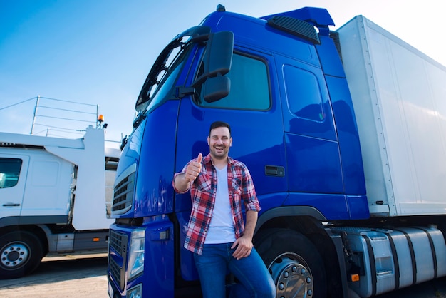 Professioneller Lkw-Fahrer vor einem langen Transportfahrzeug, das die Daumen für eine neue Fahrt bereit hält