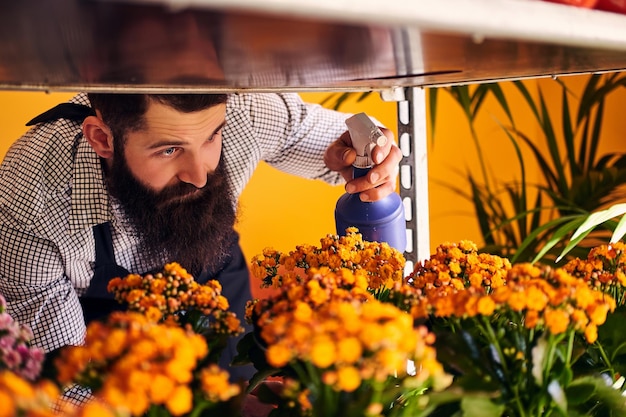 Kostenloses Foto professioneller männlicher florist mit bart und tattoo auf der hand, der eine uniform trägt, die sich in einem modernen blumenladen um blumen kümmert.