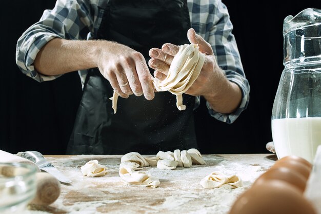 Professioneller männlicher Koch besprüht Teig mit Mehl, Preapares oder backt Brot am Küchentisch