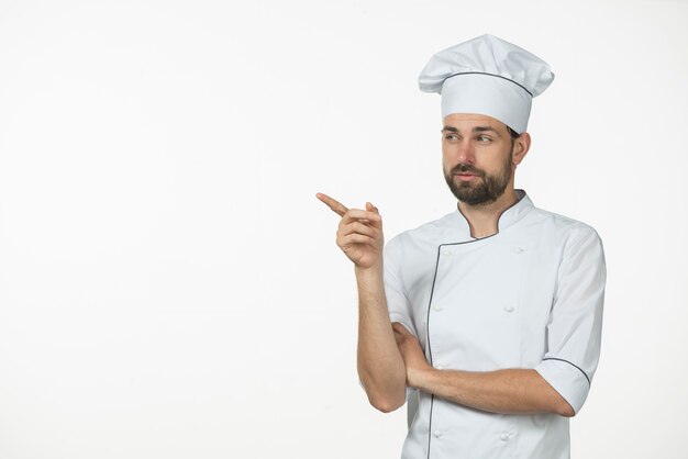 Professioneller männlicher Koch, der gegen den weißen Hintergrund zeigt auf etwas steht