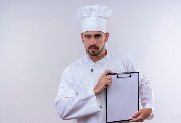 Professioneller männlicher Koch kocht in der weißen Uniform und im Kochhut, der Zwischenablage mit leeren Seiten demonstriert, die über weißem Hintergrund stehen