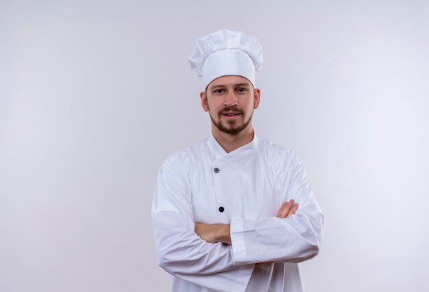 Professioneller männlicher Koch kocht in der weißen Uniform und im Kochhut mit den verschränkten Armen, die zuversichtlich über weißem Hintergrund stehen