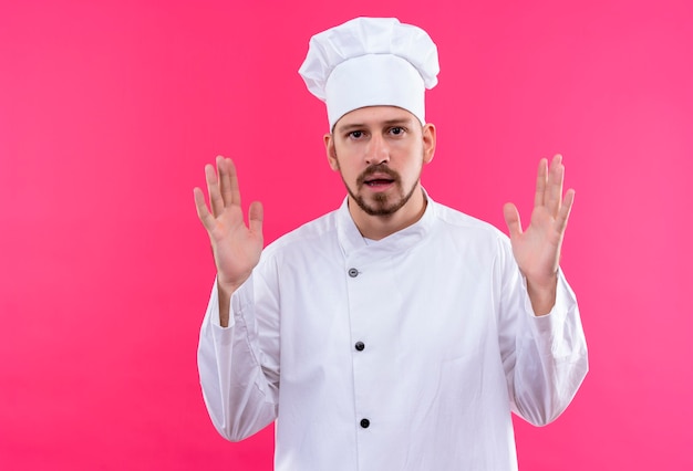 Professioneller männlicher Kochkoch in der weißen Uniform und im Kochhut gestikulierend mit den Händen, die Größe zeigen, messen Symbol über rosa Hintergrund