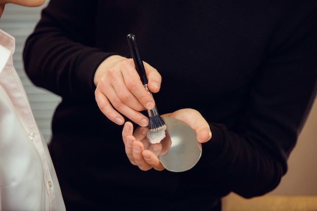 Professioneller Maskenbildner, der im Salon arbeitet. Der Mann im weiblichen Beruf. Konzept der Gleichstellung der Geschlechter. Männliche Hände mit Bürstennahaufnahme