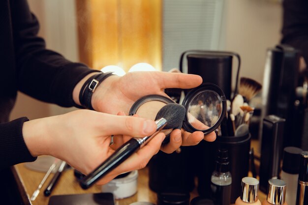 Professioneller Maskenbildner, der im Salon arbeitet. Der Mann im weiblichen Beruf. Konzept der Gleichstellung der Geschlechter. Männliche Hände mit Bürstennahaufnahme