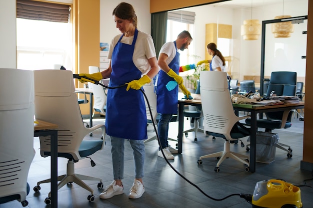 Kostenloses Foto professioneller reinigungsdienstmitarbeiter, der im büro einen staubsauger verwendet