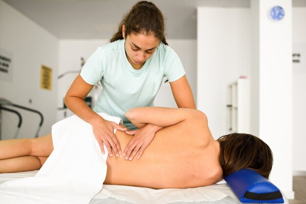 Professioneller weiblicher Physiotherapeut, der einer Frau lumbale Schultermassage gibt