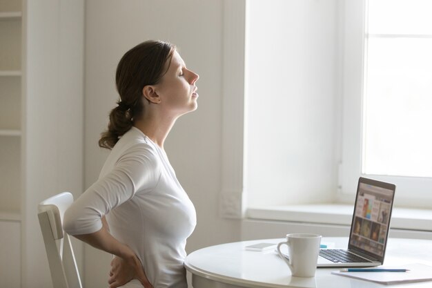 Profil Porträt einer Frau am Schreibtisch Dehnen, Rückenschmerzen Positio