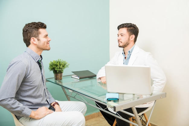 Kostenloses Foto profilansicht eines jungen männlichen ernährungsberaters, der mit einem patienten in seinem büro in einer gesundheits- und spa-klinik spricht