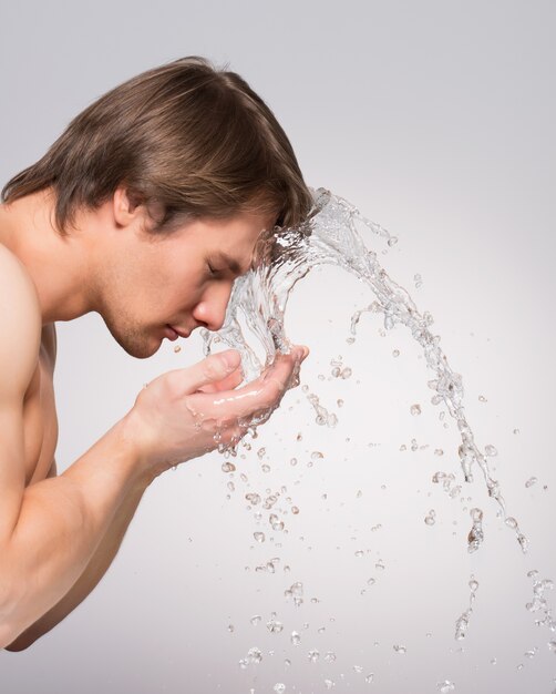 Profilporträt eines gutaussehenden Mannes, der sein Gesicht mit Wasser auf grauer Wand wäscht.