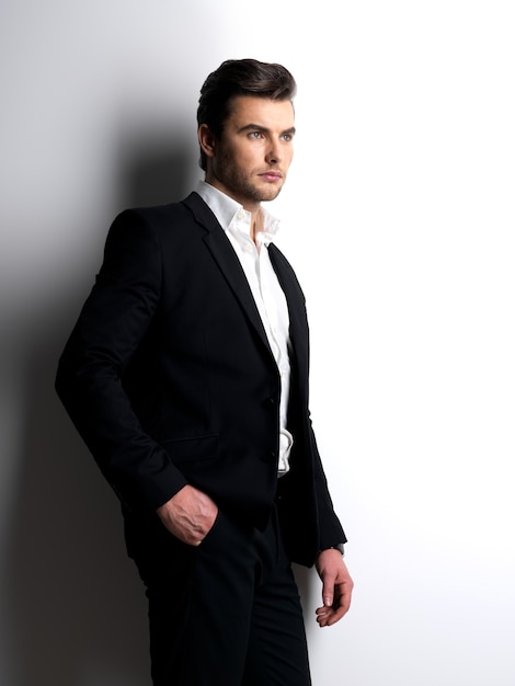 Profilporträt eines jungen Mode-Mannes im schwarzen Anzug, der im Studio aufwirft