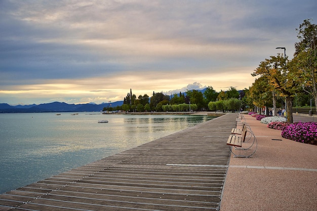 Promenadenpier von Bardolino, Gardasee mit Bänken, Blumen, Bäumen, Wasser und dramatischem Abendhimmel