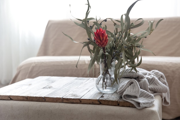 Protea-Blume in einer Glasvase und einem gestrickten Element auf dem Tisch im Raum.