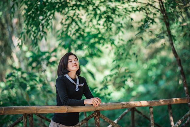 Protrait junge Frau, die auf Bambusbrücke steht, lächelt und sieht schöne Natur aus, während sie im Wald mit glücklichem Kopienraum kampiert