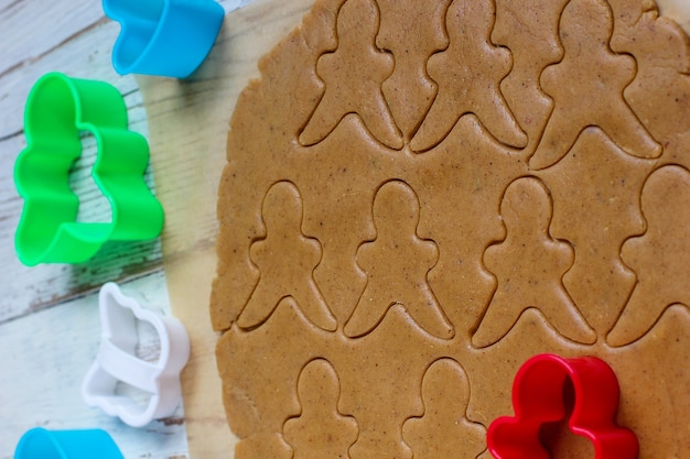 Prozess der Behandlung von Lebkuchenmannplätzchen, benutzen roten Lebkuchenmann-Formausschnitt-Lebkuchenteig auf Backpapier um bunte Ausstechformen auf weißem Holztisch. Ansicht von oben