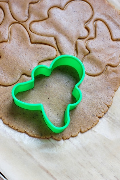 Prozess der Behandlung von Lebkuchenmannplätzchen, benutzen roten Lebkuchenmann-Formausschnitt-Lebkuchenteig auf Backpapier um bunte Ausstechformen auf weißem Holztisch. Ansicht von oben