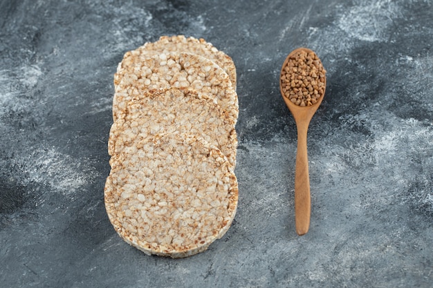 Puffed Crispbread und Holzlöffel rohen Buchweizens auf Marmoroberfläche