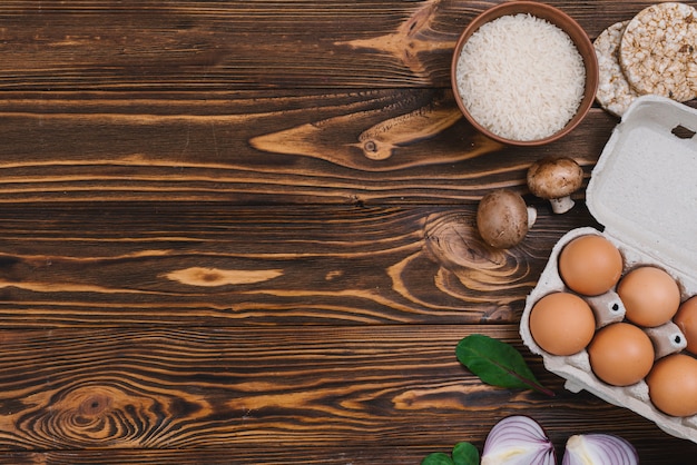 Puffreis; Reiskörner; Pilz; Eier und Zwiebeln über Schreibtisch aus Holz