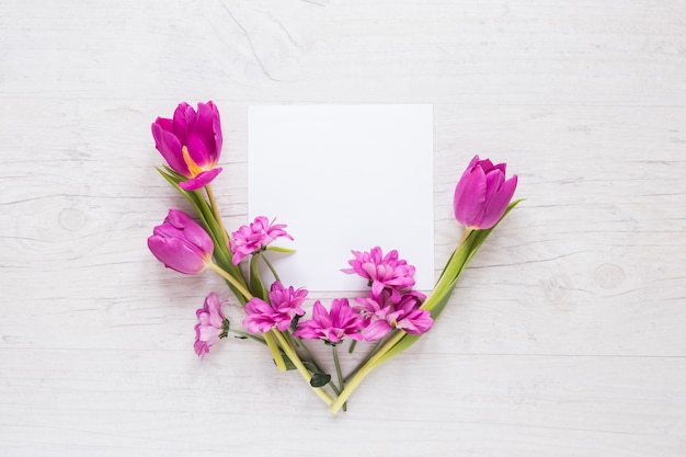 Purpurrote Blumen mit leerem Papier auf Tabelle