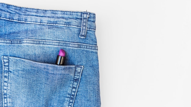 Purpurroter Lippenstift in den Blue Jeanstaschen über weißem Hintergrund