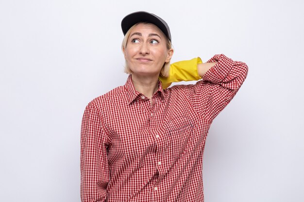 Putzfrau in kariertem Hemd und Mütze mit Gummihandschuhen, die verwirrt aufschaut
